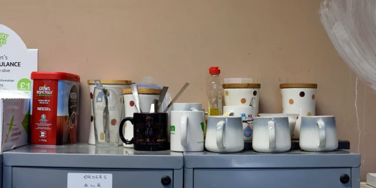 Workers' mugs, spoons and tea stored on top of filing cabinet