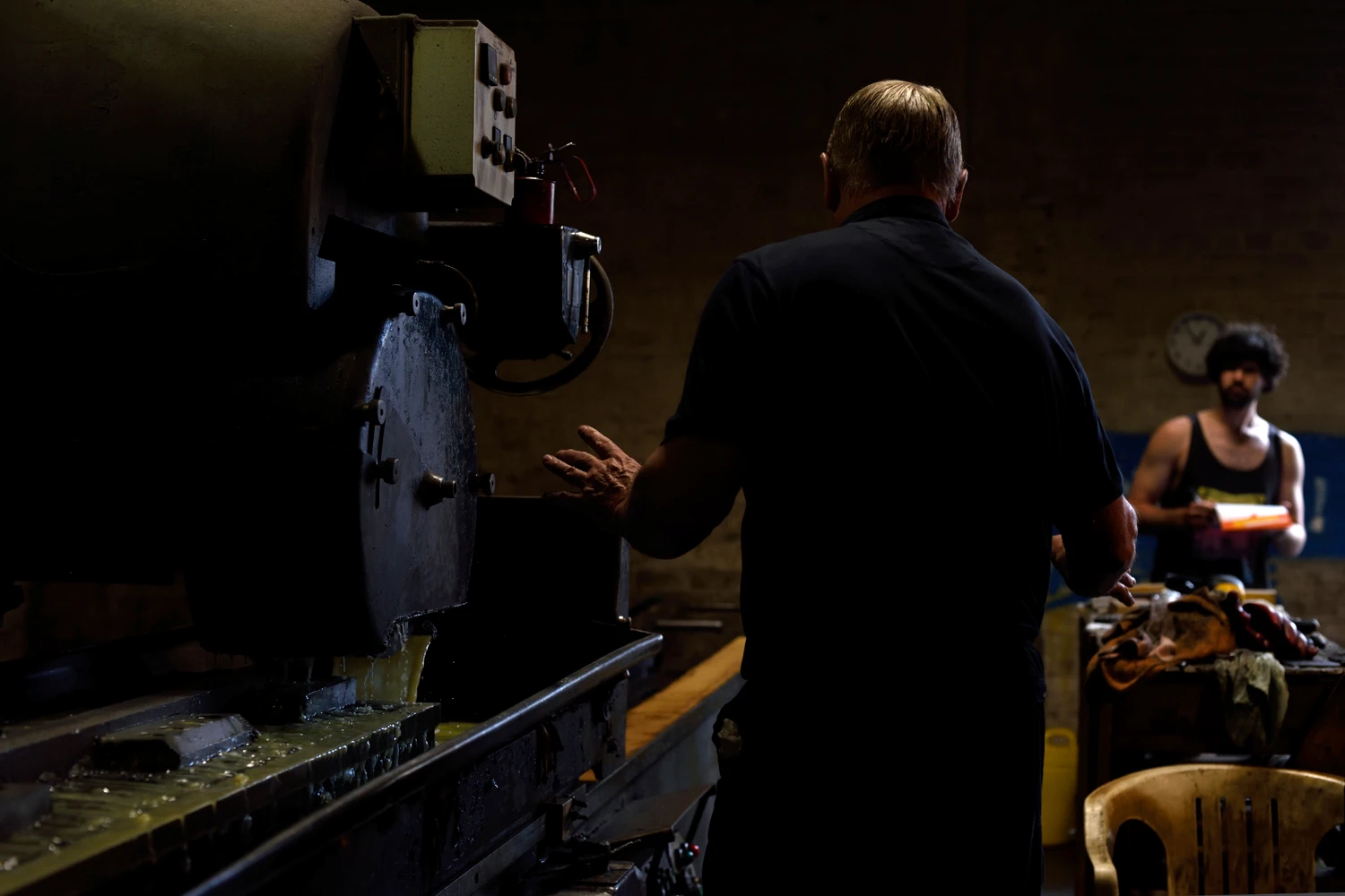 Machine rinses steel as older man instructs an apprentice in factory