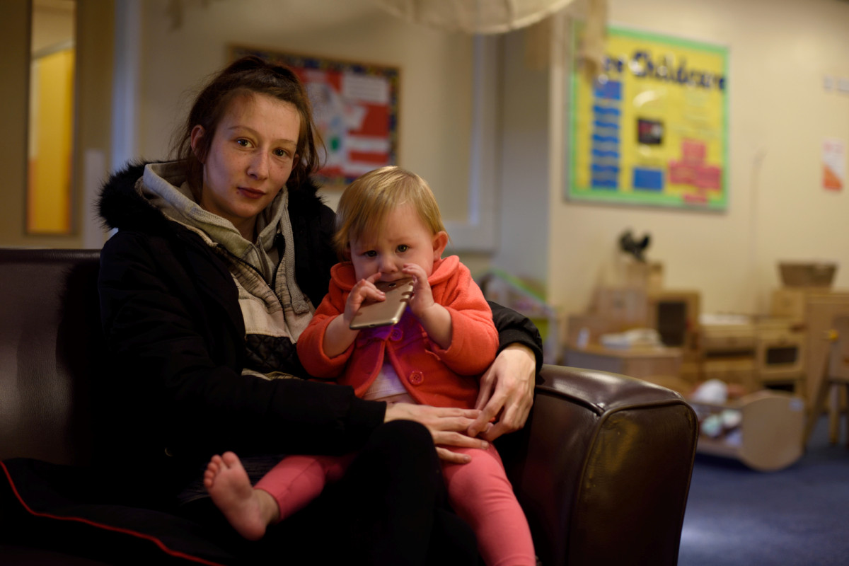 A young mother with toddler chewing phone case on her knee