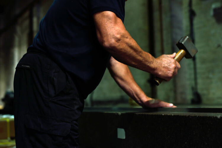 the arms of a man using a large hammer to work a piece of steel