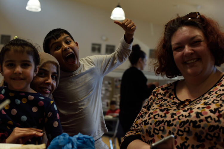 Brown mother and two children with a white neighbour sitting at a table smiling and facing camera