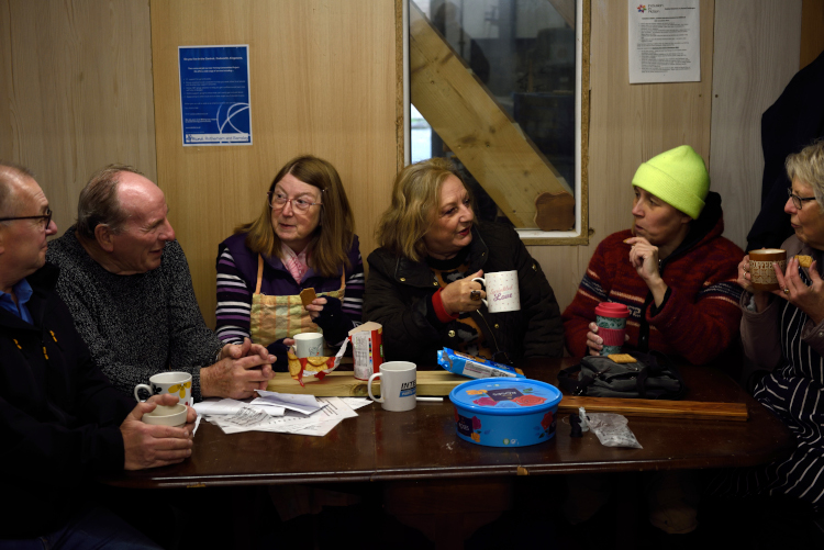 group of people chatting animatedly over tea and biscuits around a table