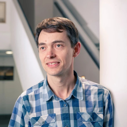 A head and shoulders picture of a man in a checked shirt with brown hair who is smiling