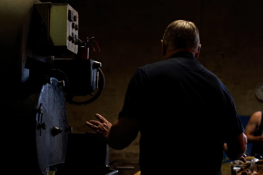 Machine rinses steel as older man instructs an apprentice in factory