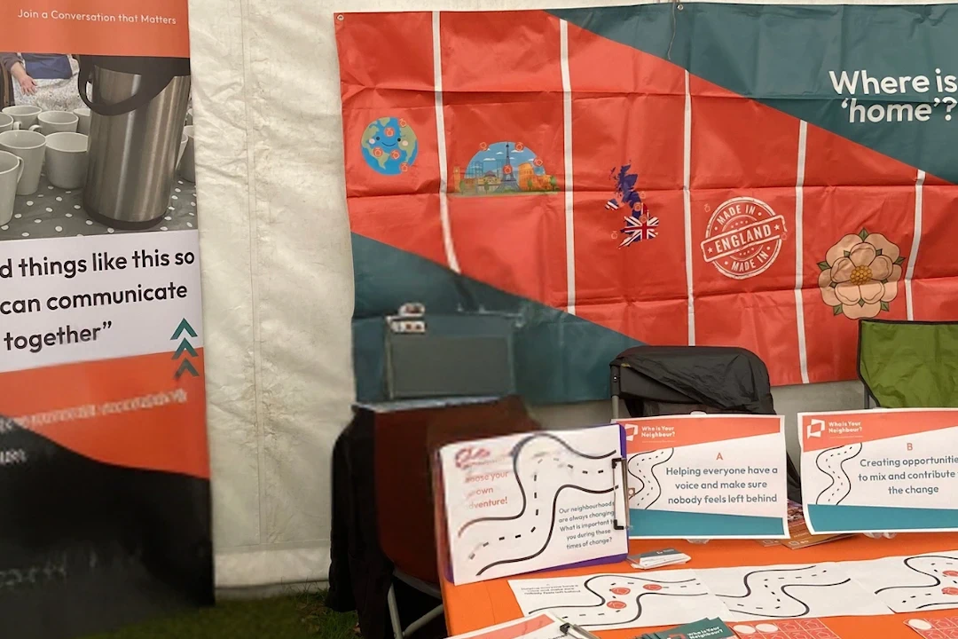 table and banners at a Who is Your Neighbour? pop-up event in the summer of 2026